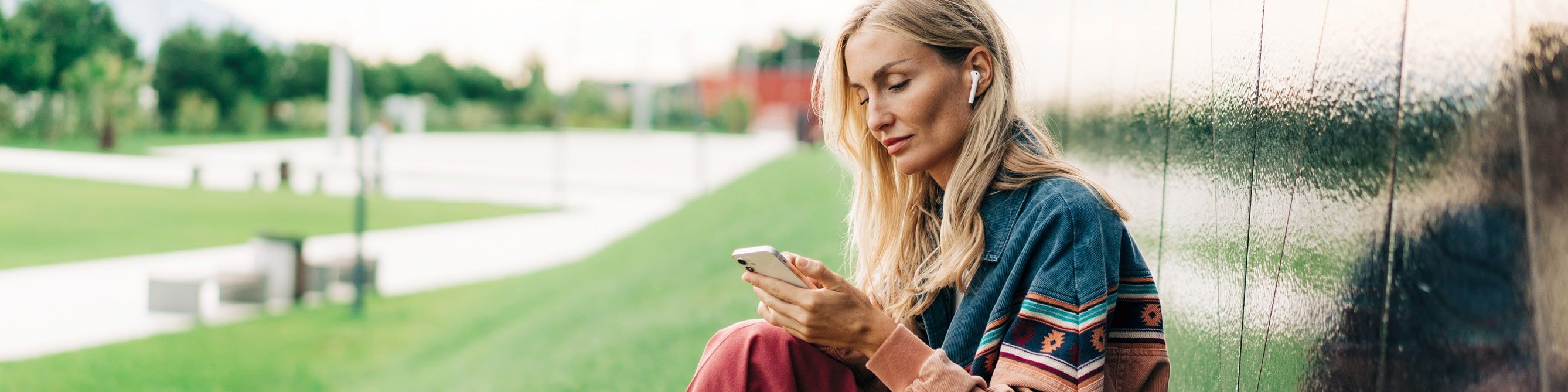 Frau sitzt auf dem Rasen und schaut auf ihr Smartphone