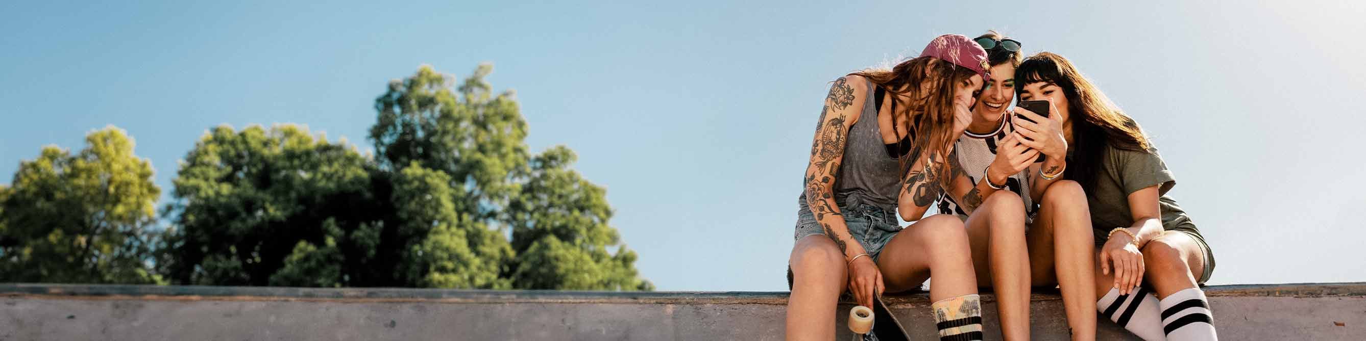 Handyversicherung: Drei Frauen an einer Skaterrampe schauen auf ein Smartphone 