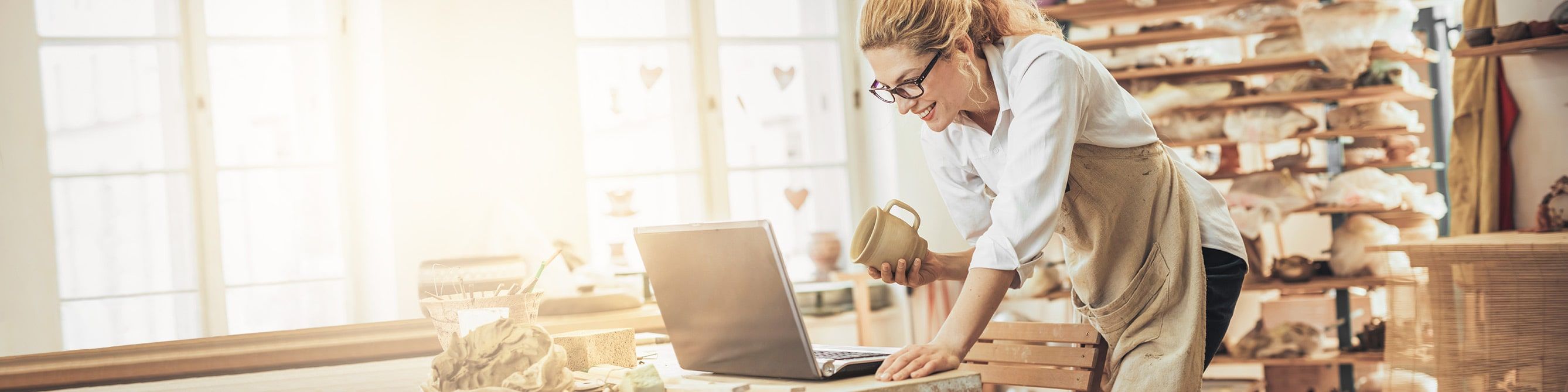Firmenkundin in ihrer Töpferei informiert sich am Laptop über Versicherungen für den Einzelhandel