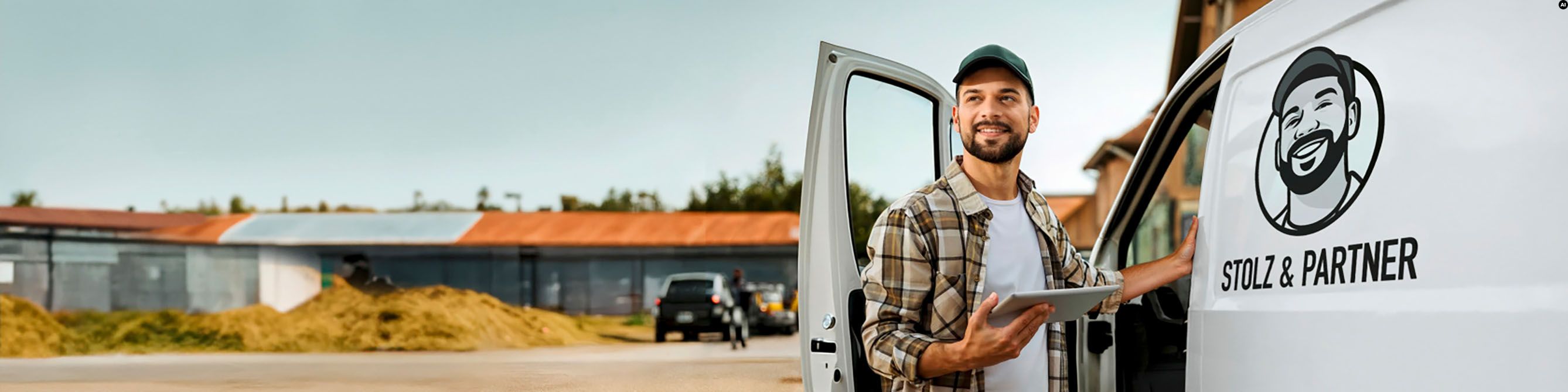 Ein junger Mann in Arbeitskleidung steht vor der geöffneten Tür seines Kleintransporters