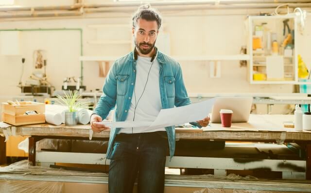 Ein Mann steht in einem atelierähnlichen Büro, er hält einen großen Plan in der Hand.