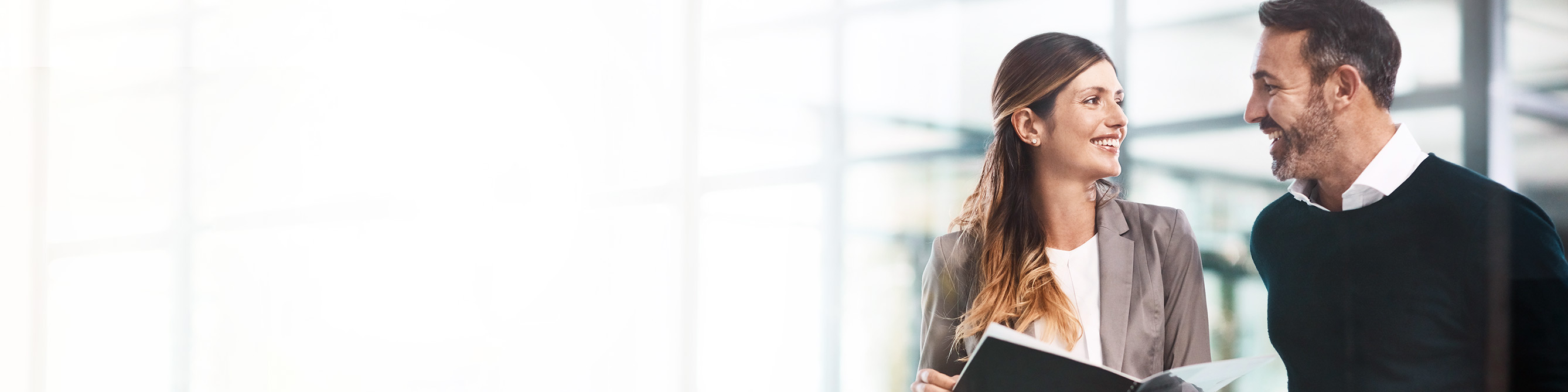 Ein Man und eine Frau schauen sich an und lächeln, die Frau hält ein Dokument in ihren Händen.