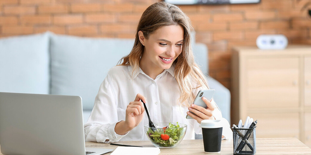 Frau isst Salat und chaut aufs Handy