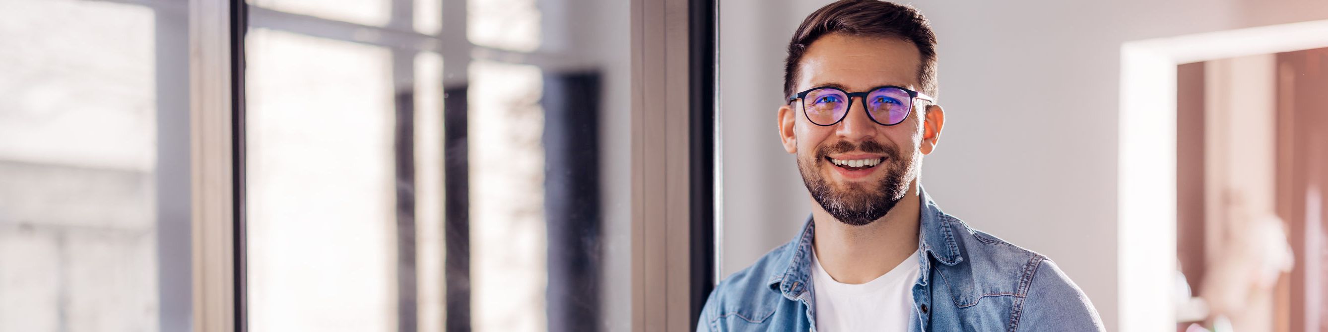 Mann mit Brille steht lachend in seinem Wohnbereich.