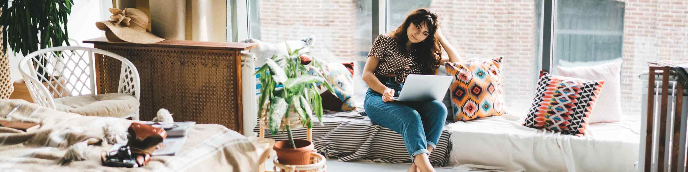 Frau sitzt auf Couch vor Fensterfront mit Laptop