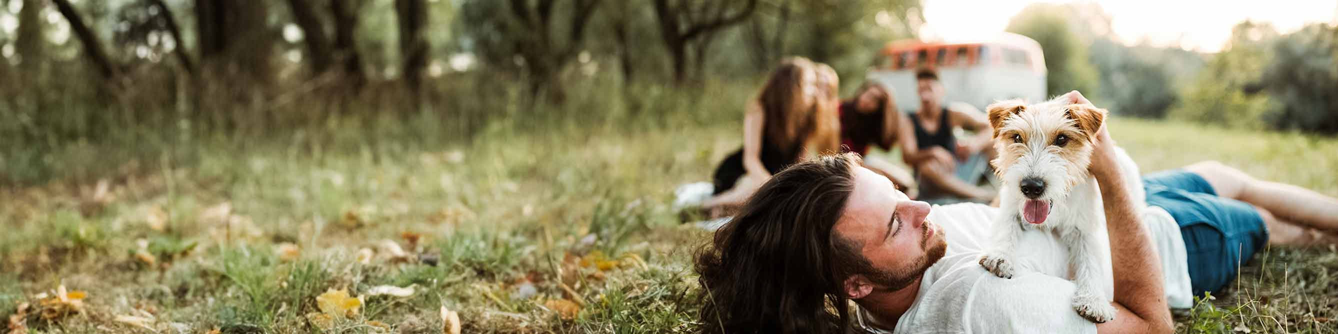 Frau liegt mit ihrem Hund auf einer Wiese 
