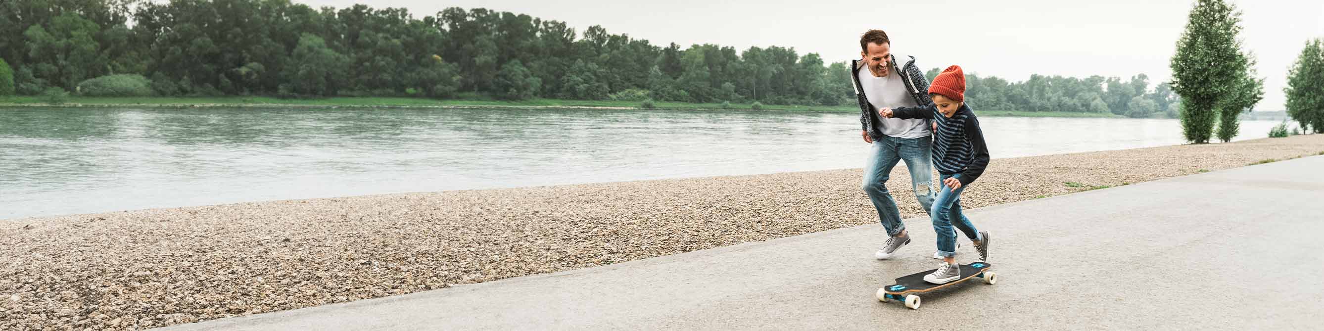 Kind fährt Skateboard und Vater rennt nebenher