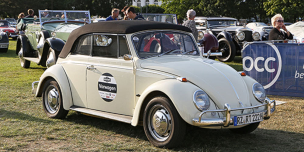 Ein altes VW Käfer Cabrio in weiß mit dunklem Verdeck ist zu sehen.