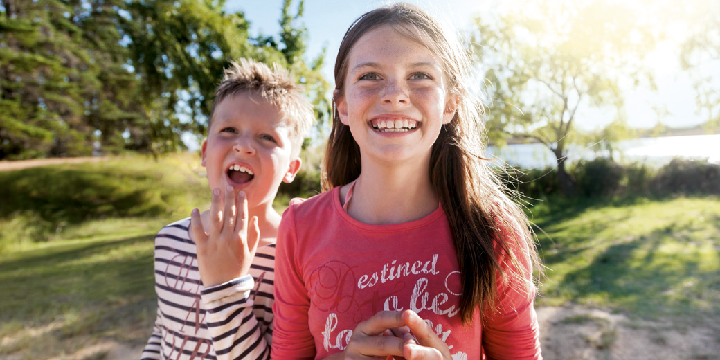 Zwei Kinder spielen im Garten und schauen lachend in die Kamera.
