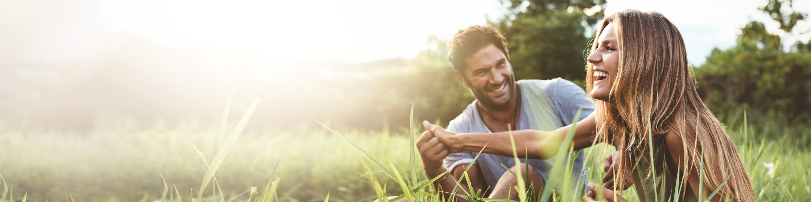 Ein junger Mann und eine junge Frau sitzen im Gras und lachen sich an.