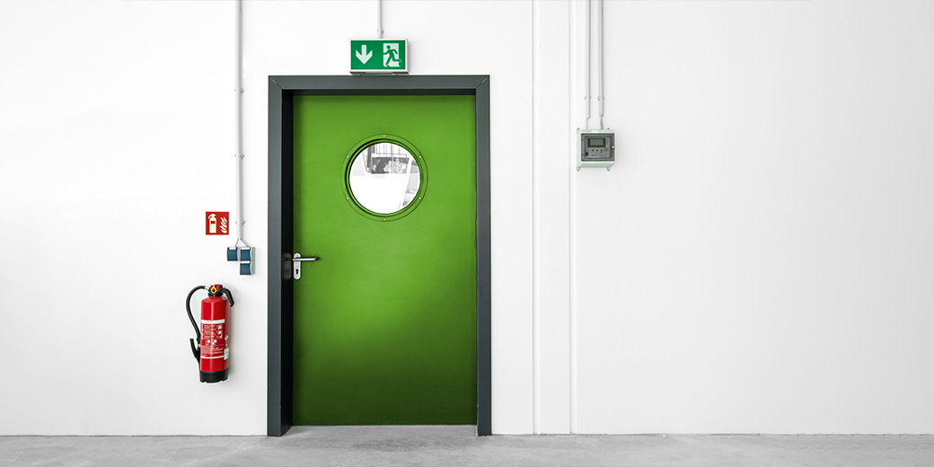 Das Bild zeigt einen Feuerlöscher, der an eine Wand neben einer Tür angebracht ist.