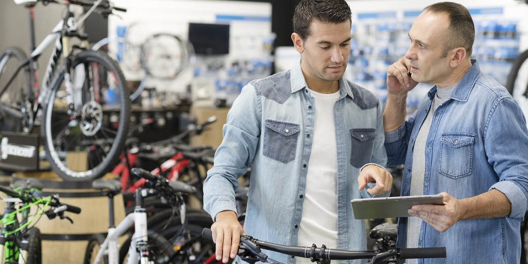 Zwei Männer stehen in einem Fahrradladen und diskutieren, einer hält ein Tablet in der Hand.