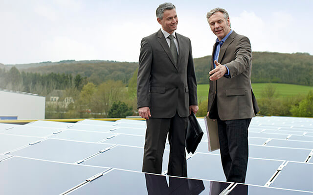 Der Betreiber einer Photovoltaik-Anlage steht mit einem Berater im Anzug inmitten der Kollektoren.