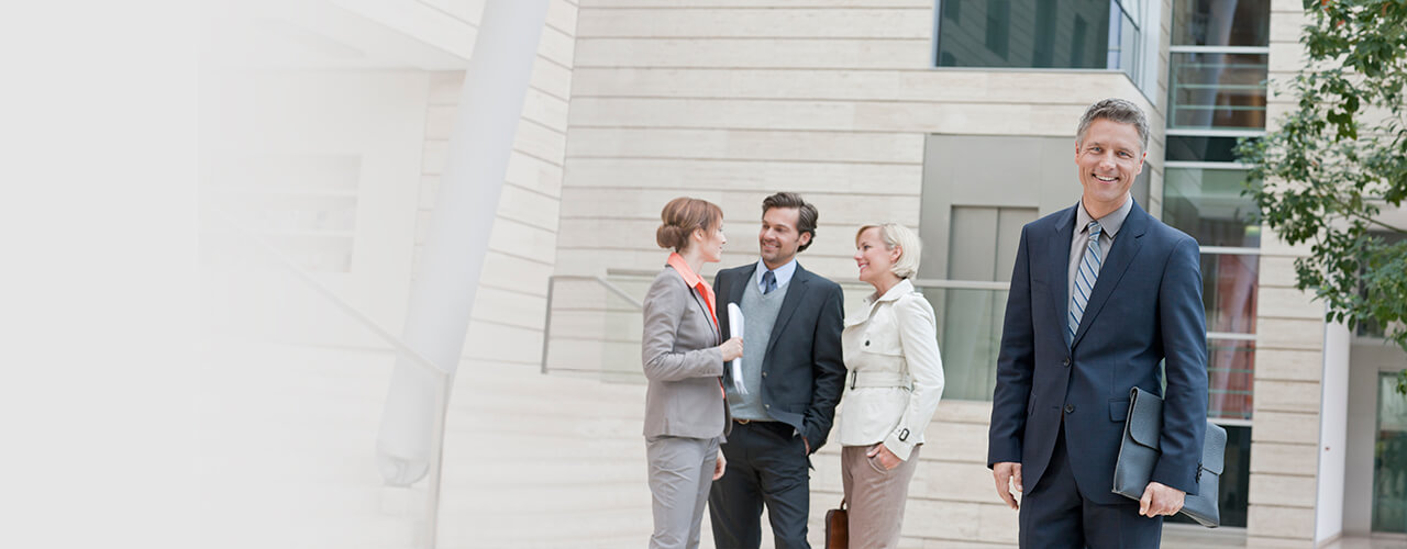 Vertrauensschadenversicherung: Das Bild zeigt einen im Anzug, im Hintergrund spricht ein Mann mit zwei Frauen.