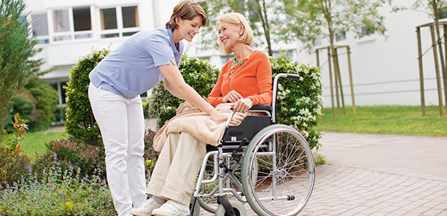 SofortRente Pflege: Ein Pflegerin hilft einer Patientin im Rollstuhl.
